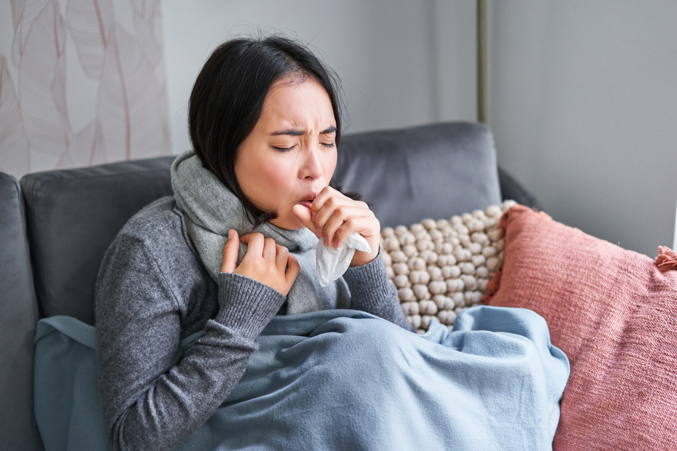 donna asiatica che tossisce sentirsi male seduto sotto coperta con scard in appartamento freddo risparmiando su heati scaled